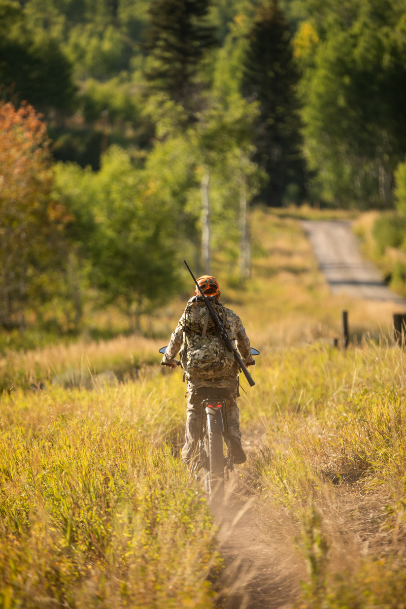 Man Riding Off on E-Bike with Rifle