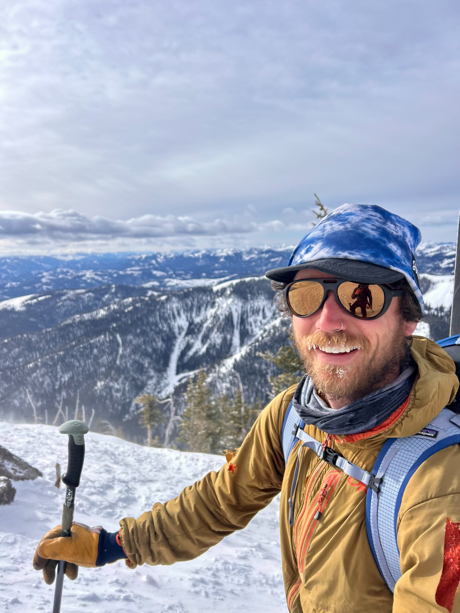A person wearing Costa Del Mar sunglasses looks out over the scenic overlook at Teton Pass. The polarized lenses reflect the dramatic mountain landscape of the Teton Range. The image captures the 'Teton Tested' durability of the frames in a high-elevation backcountry environment.