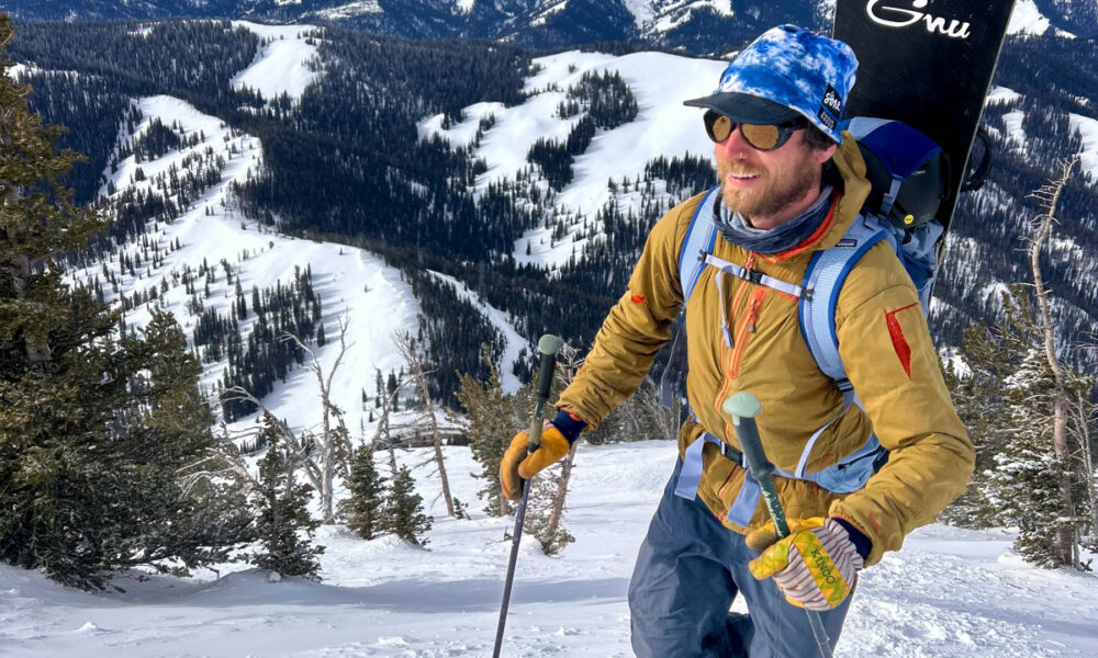 A person wearing Costa Del Mar sunglasses looks out over the scenic overlook at Teton Pass. The polarized lenses reflect the dramatic mountain landscape of the Teton Range. The image captures the 'Teton Tested' durability of the frames in a high-elevation backcountry environment.