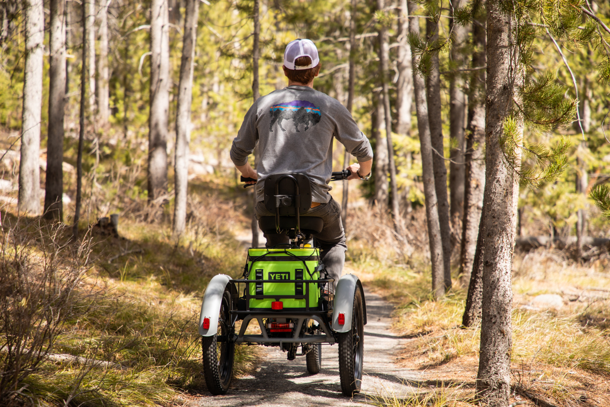 Rear view of a man riding a Mooncool TK2 e-trike down a wooded path showing the triple rear safety lights.