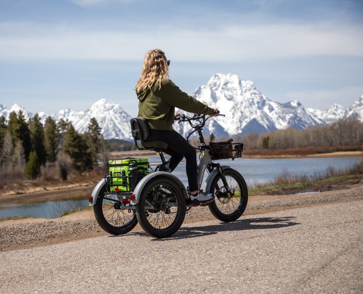Side view of a rider on the Mooncool TK2 electric tricycle near a scenic mountain lake.