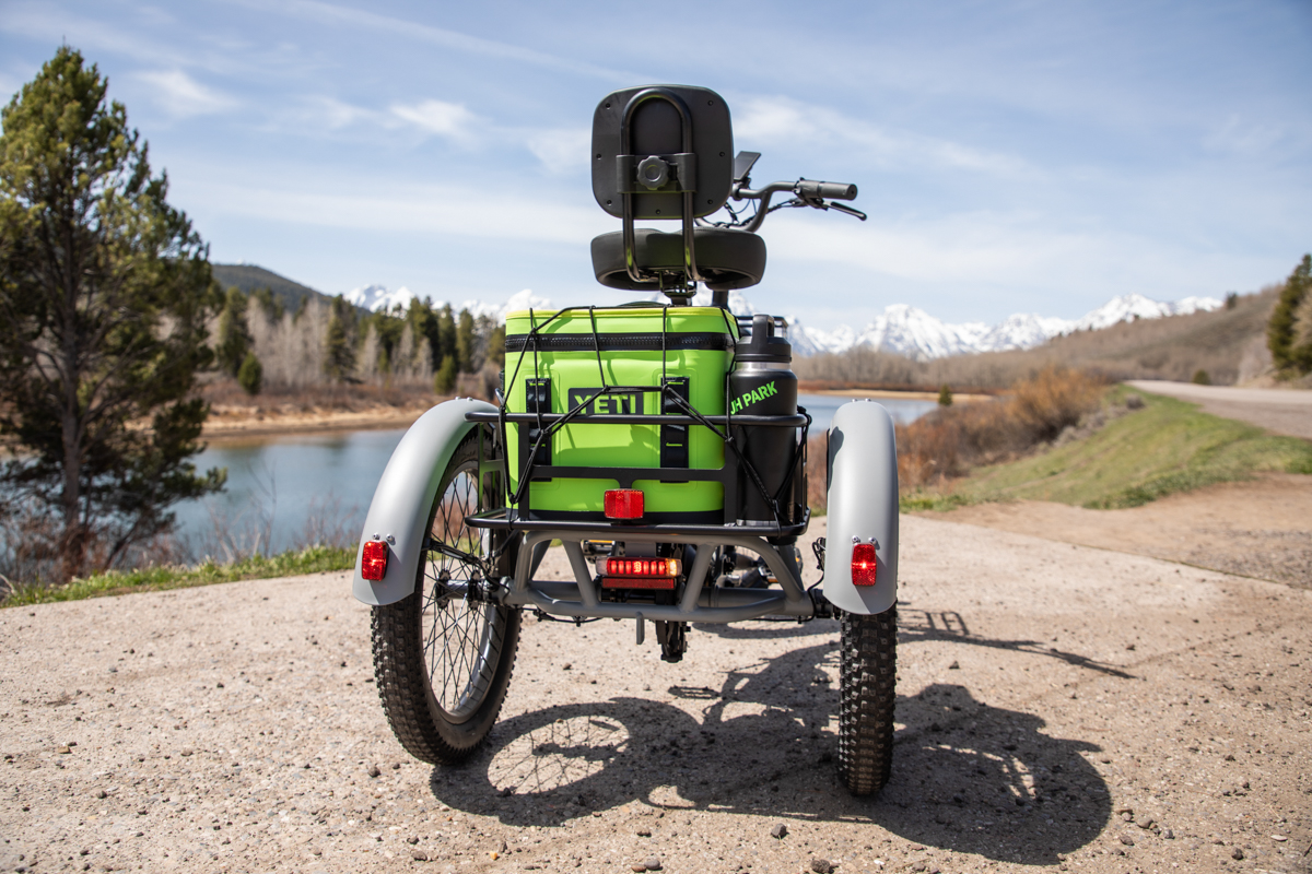 Rear view of the Mooncool TK2 electric tricycle showing the large rear cargo basket loaded with a green Yeti cooler.