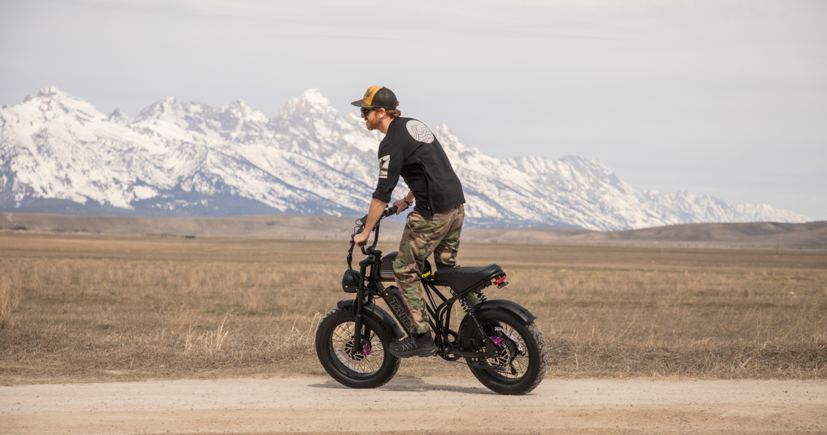 A rider testing the climbing torque of the Talon T87 Dual Motor E-Bike on a dirt slope in Jackson, Wyoming, with local Teton architecture visible in the background.
