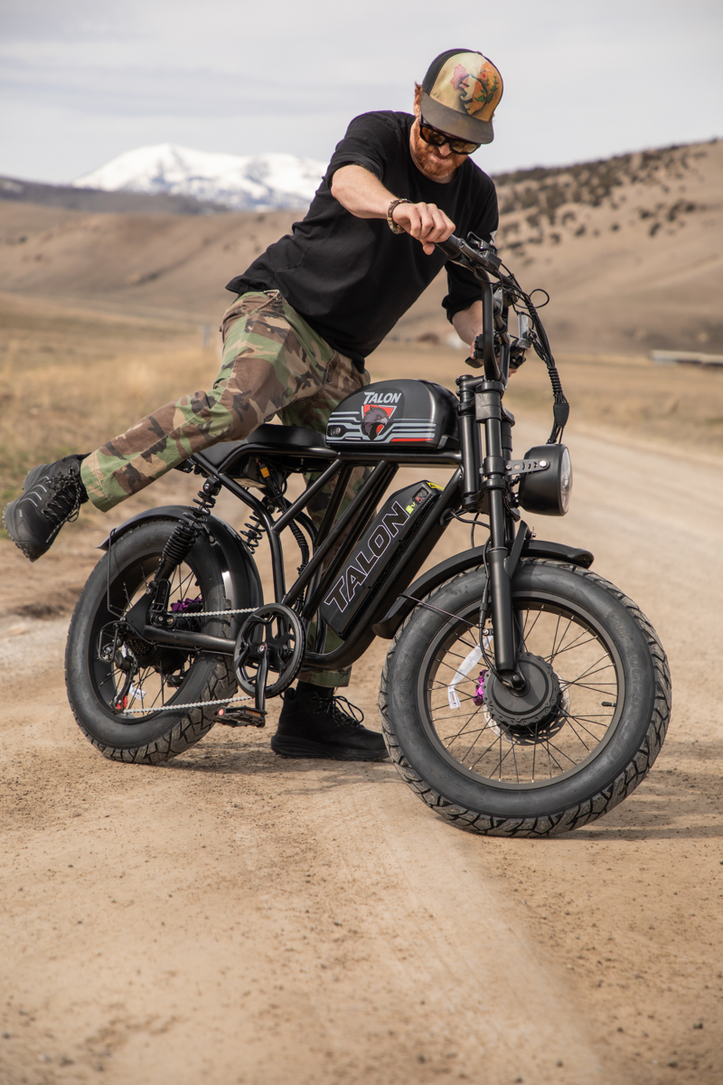 Rider preparing to ride the Talon T87 Dual Motor E-Bike on a scenic dirt road, 'Teton Tested' to ensure durability and performance in high-altitude environments.