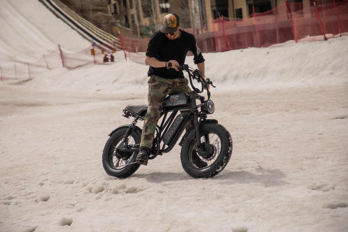 A side profile of a rider on a Talon T87 Dual Motor E-Bike on a snowy trail in Wyoming, showcasing the fat tires and dual motor hub system designed for off-road terrain.