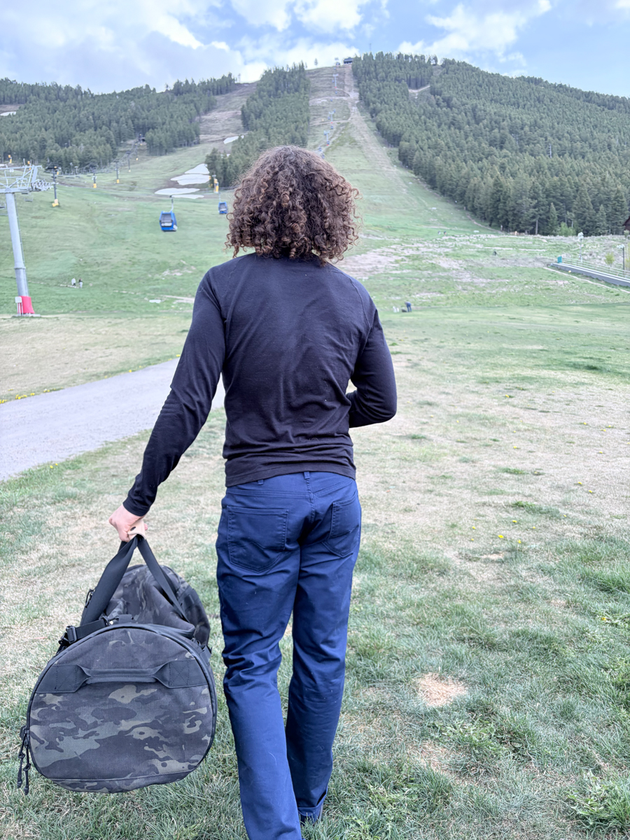 Gear tester Pat Kinney walking away carrying The Brown Buffalo Duffalo travel duffel by its shoulder strap at the base area of Snow King Mountain