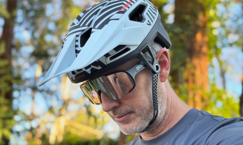 Canyon Deflectr Trail helmet featuring a three-position adjustable visor, shown with sunglasses tucked underneath to demonstrate storage integration during mountain bike trail rides.