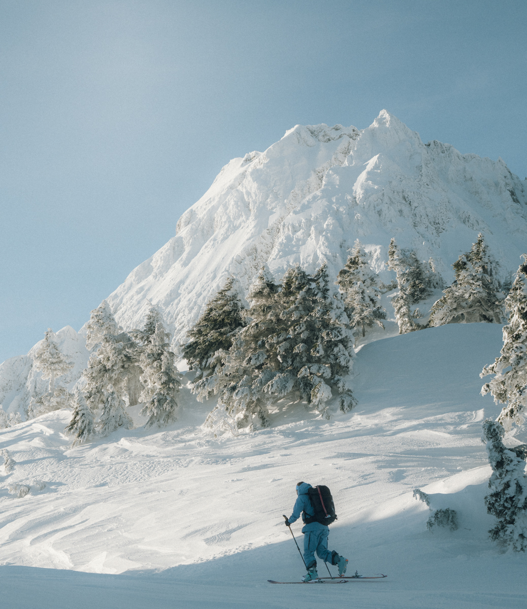 Backcountry skier walking uphill in the backcountry wearing the Patagonia PowSlayer shell system, emphasizing range of motion in 80-denier recycled nylon fabric.