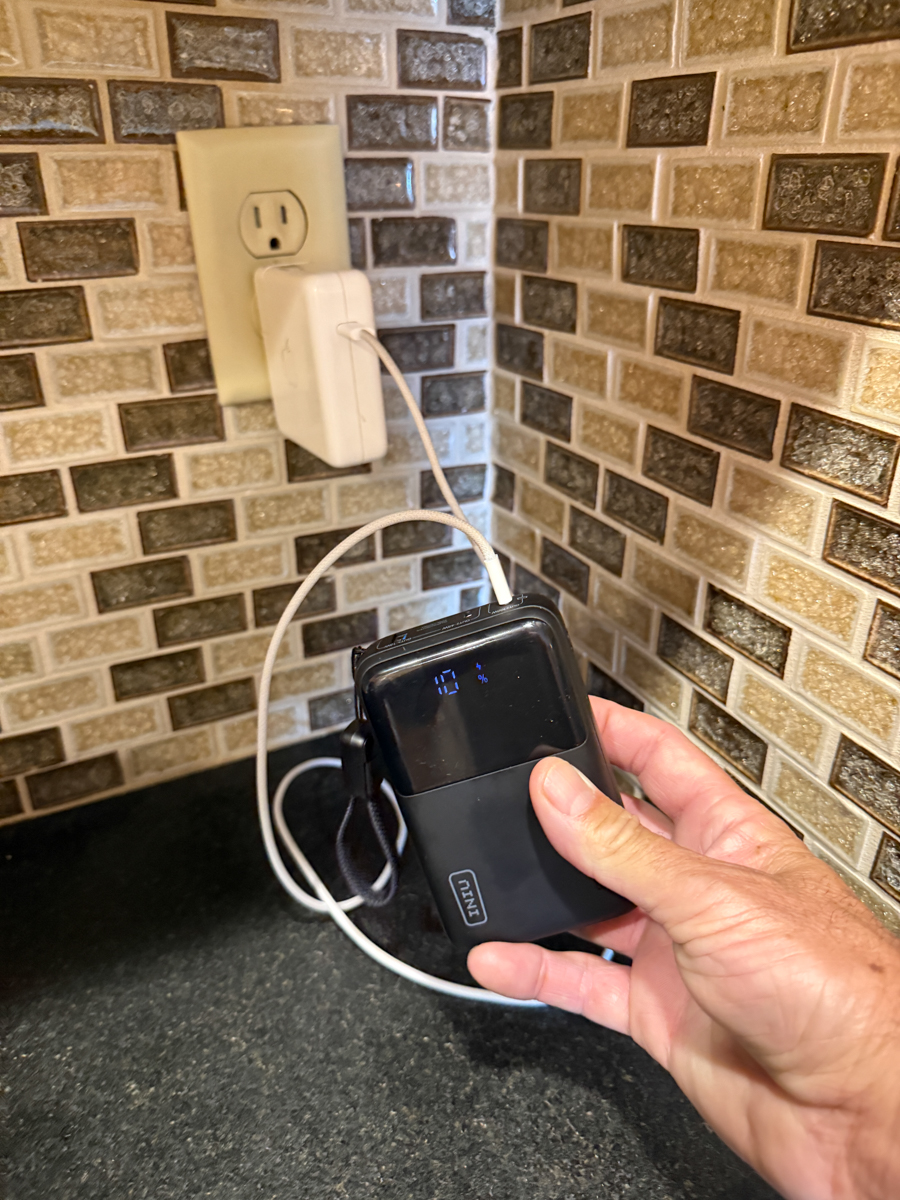 Hand plugging the INIU Cougar P63 power bank into a wall outlet for charging.