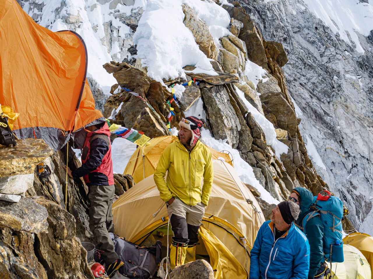 Against a backdrop of towering, icy Himalayan peaks, the expedition team fights the biting, thin air to secure their vibrant tents into the frozen snow, carving out a fragile sanctuary on the roof of the world.