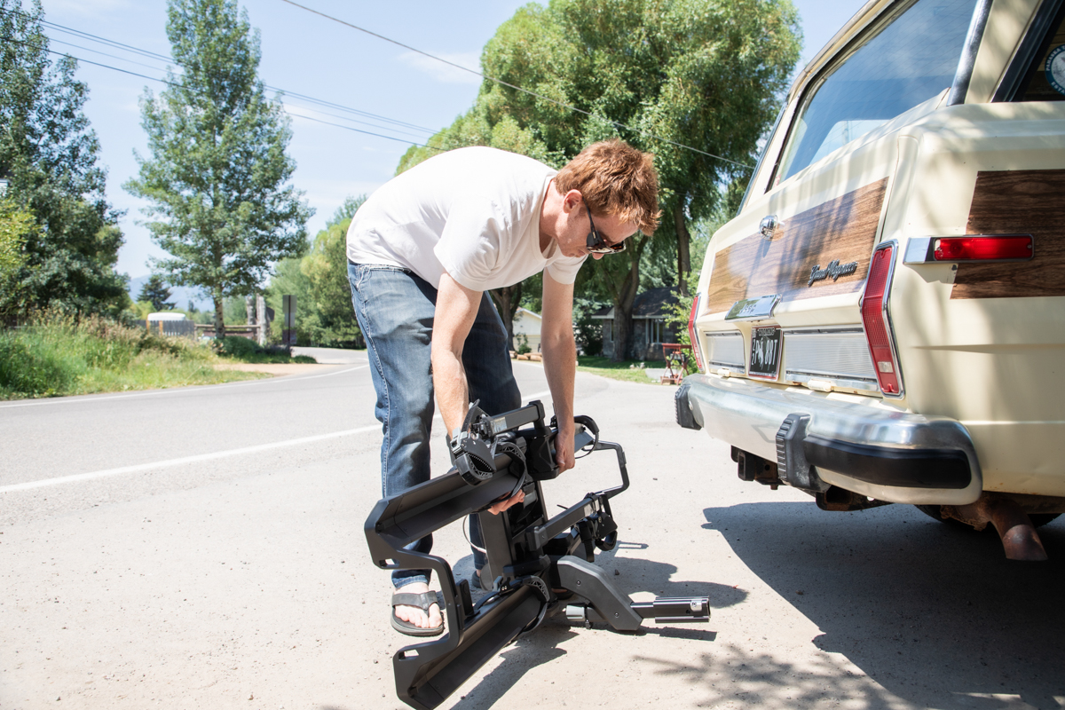 Person working near the Saris Cycle-On bike rack beside a vehicle.